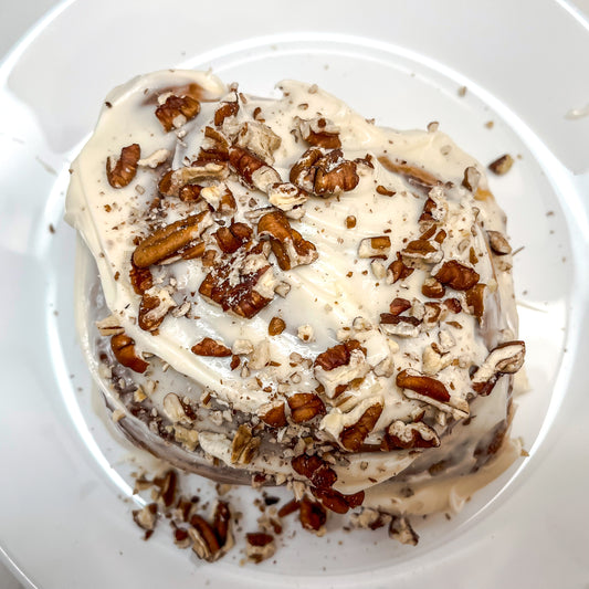 A toasted pecan cinnamon roll with vanilla cream cheese frosting, garnished with additional chopped pecans, on a plate.